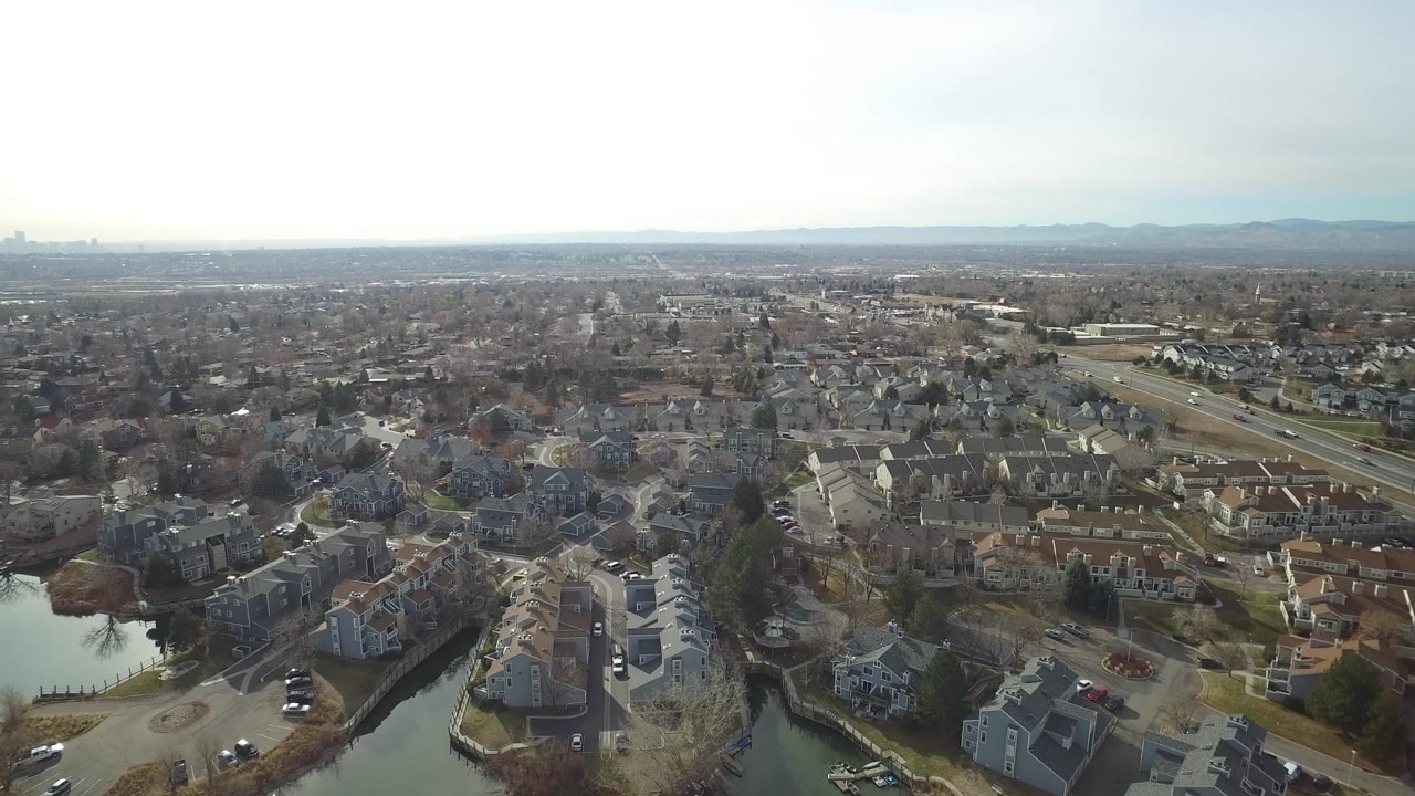 Aerial view of suburban homes, ponds, roads, and distant haze.