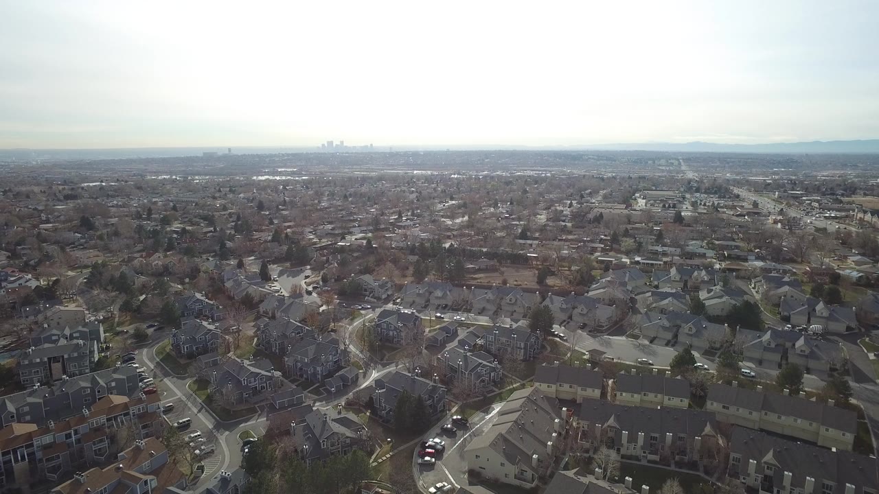 Aerial view over suburban homes and curving residential streets under a hazy sky.
