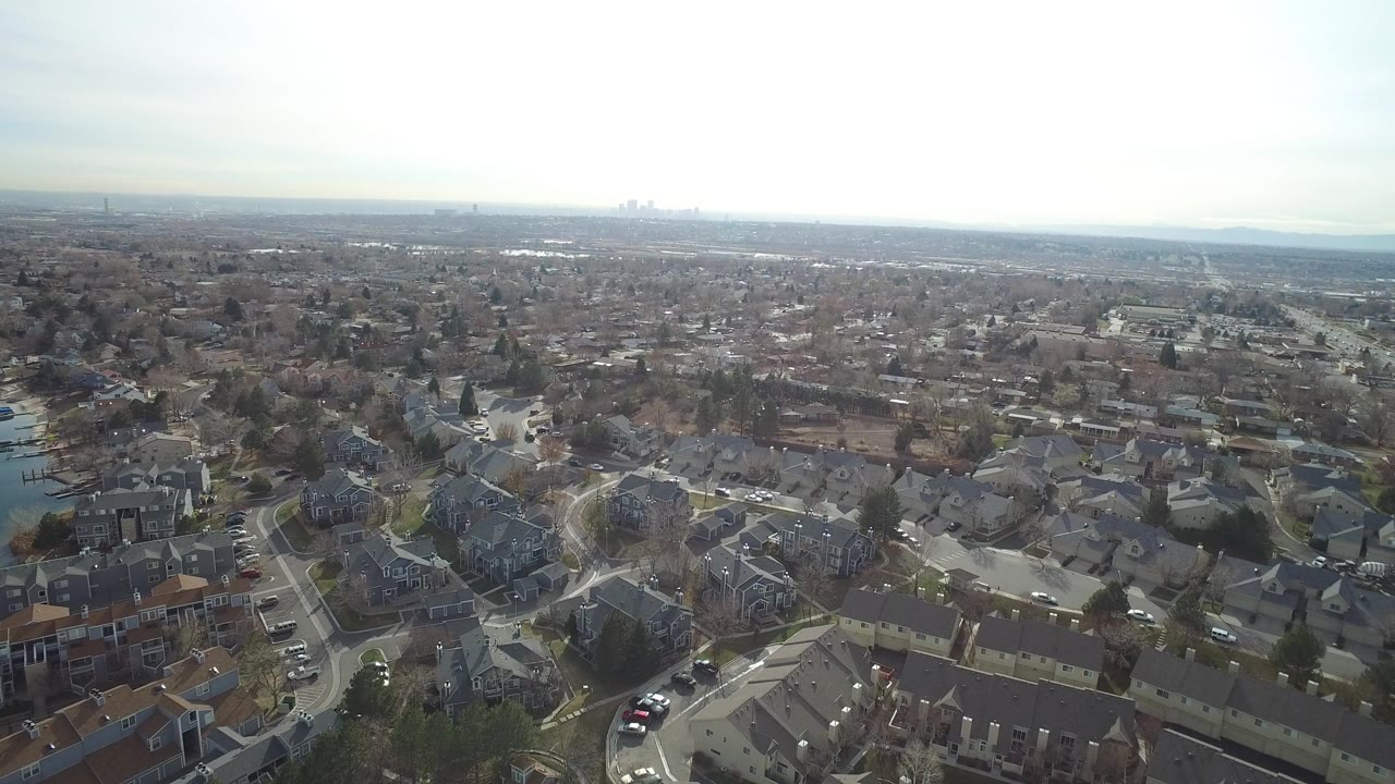 Aerial view over suburban homes, streets, water, and distant skyline.