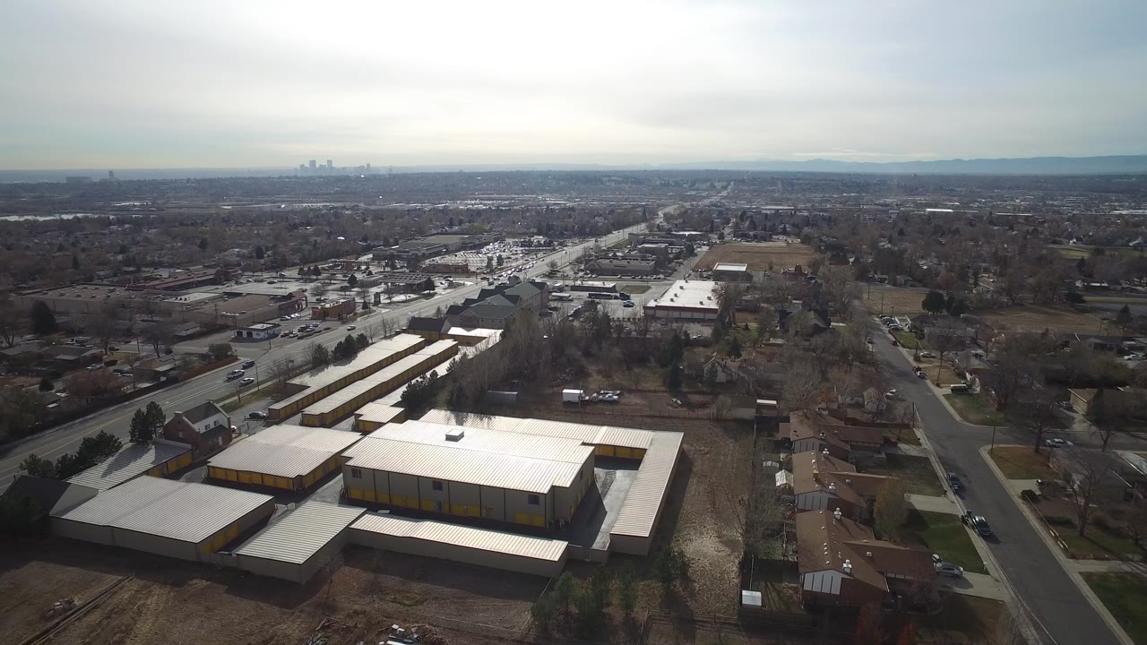 Westminster, Colorado aerial frame looking across rooftops, paved roads, parked vehicles, open lots, and a hazy skyline on the horizon with no recognizable people visible.