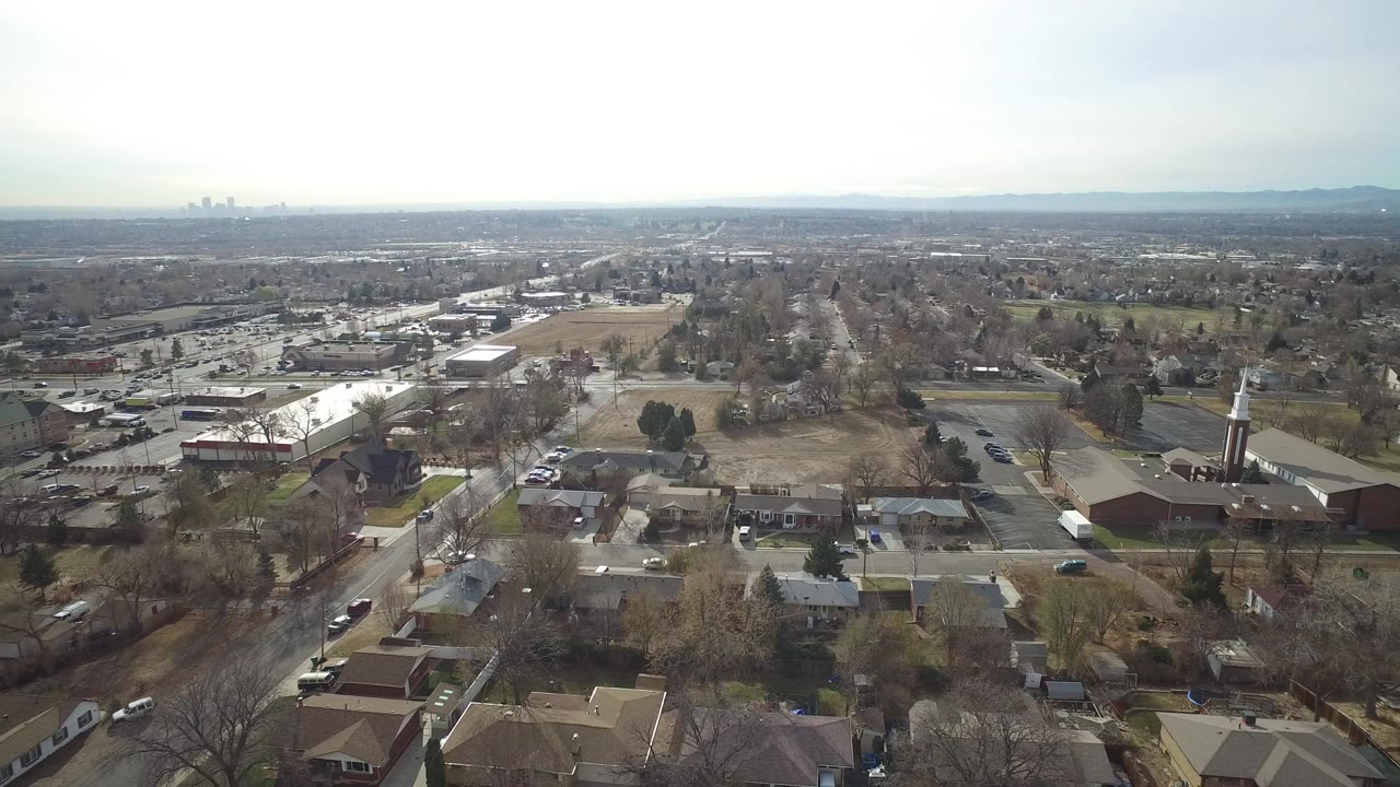 Aerial view over suburban homes, streets, trees, and a church steeple.