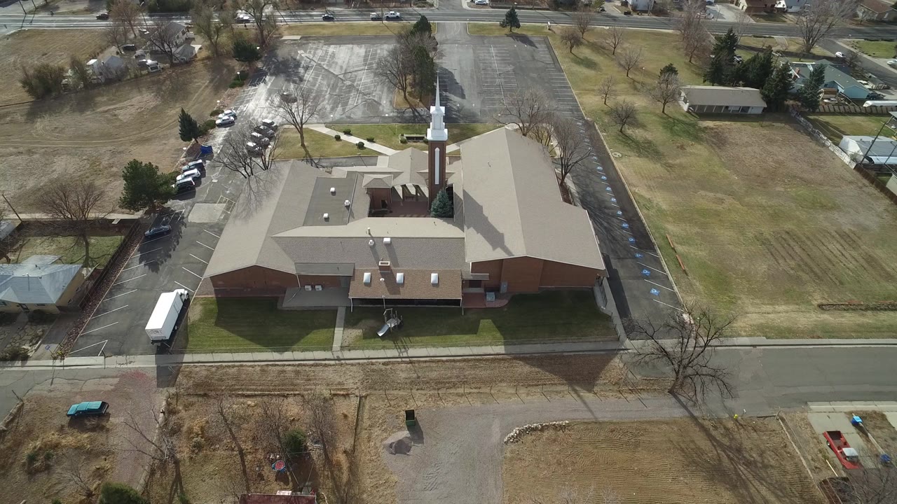 A high aerial view in Westminster, Colorado centers the church roof and white steeple, with a parking lot, bare trees, lawns, nearby houses, and no visible people.