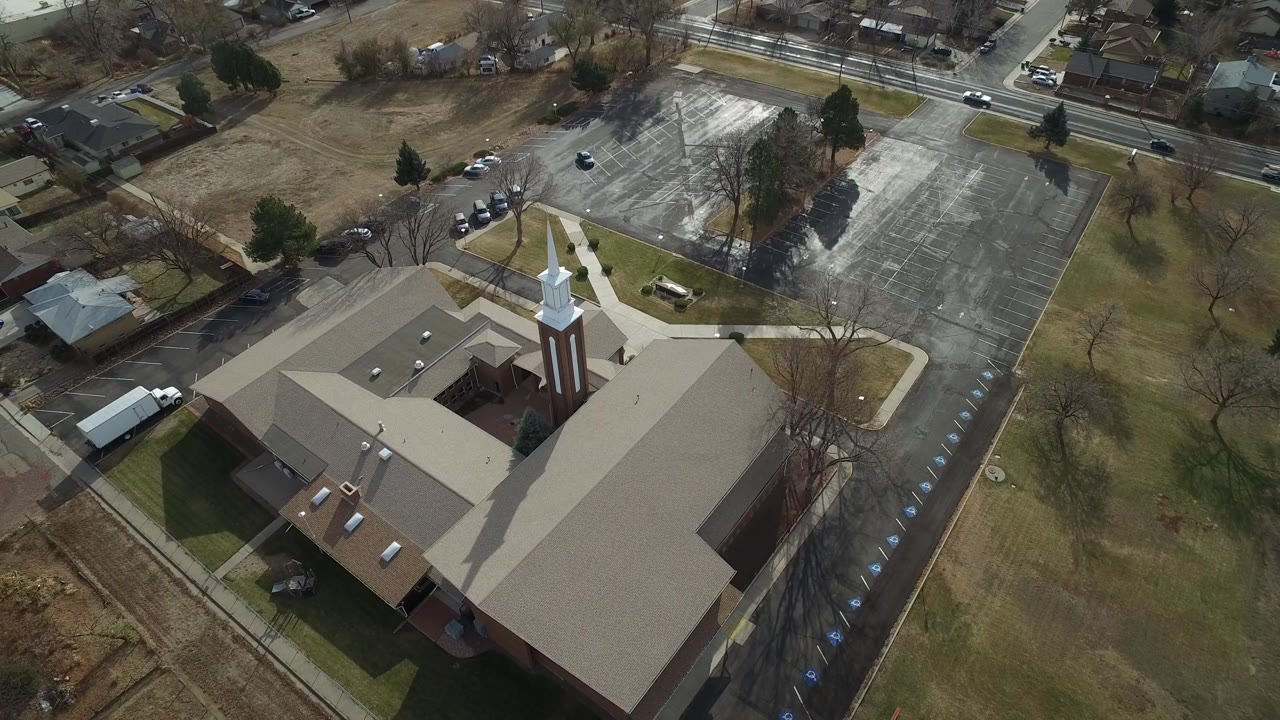 The second frame looks down on the Westminster church roof and steeple with striped parking spaces, a roadside edge, lawns, and residential buildings in view, with no visible people.