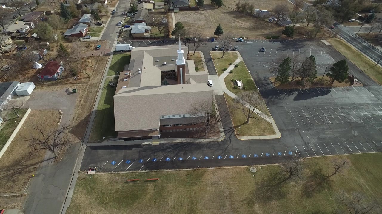 The second frame keeps the Westminster building centered, with the white steeple near the upper roofline, a wide mostly empty parking lot to the right, residential streets beyond, and no visible people.