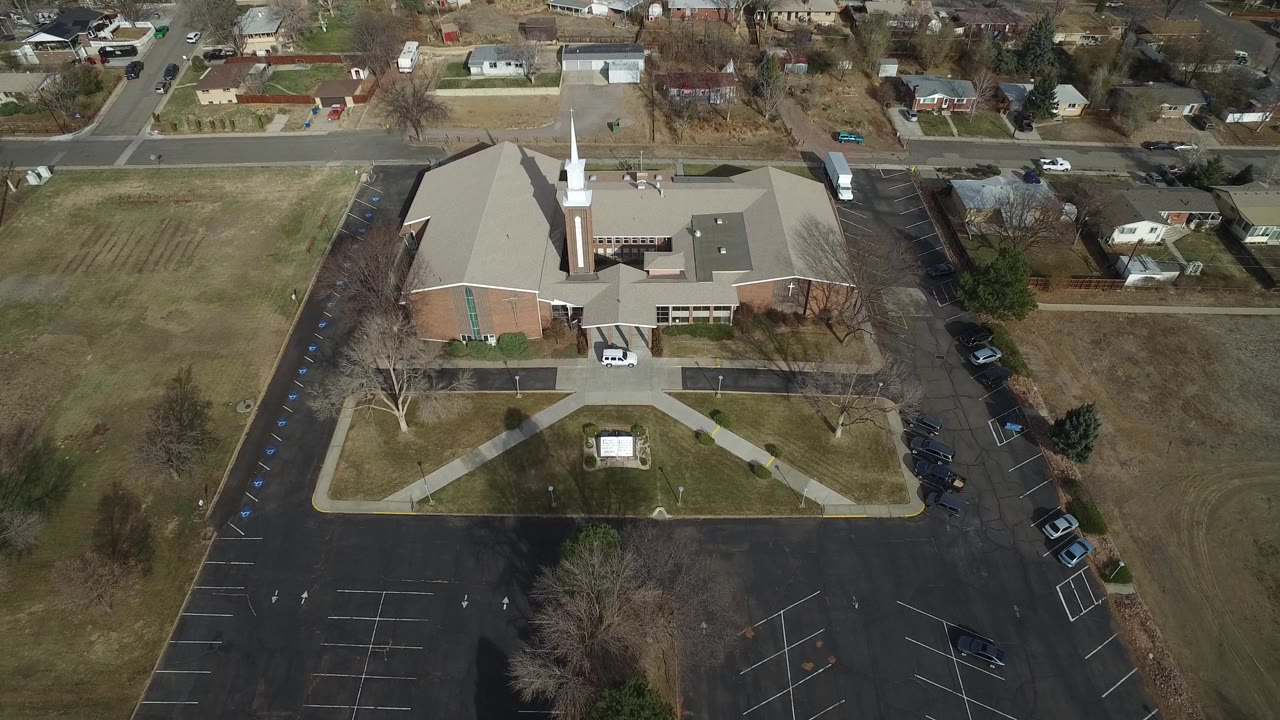 Aerial view of a large brick building with a white steeple, parking lot, lawns, and nearby houses.