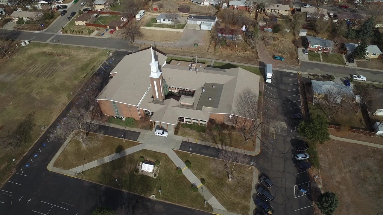 Overhead view of a church building, parking lots, streets, lawns, and nearby homes.