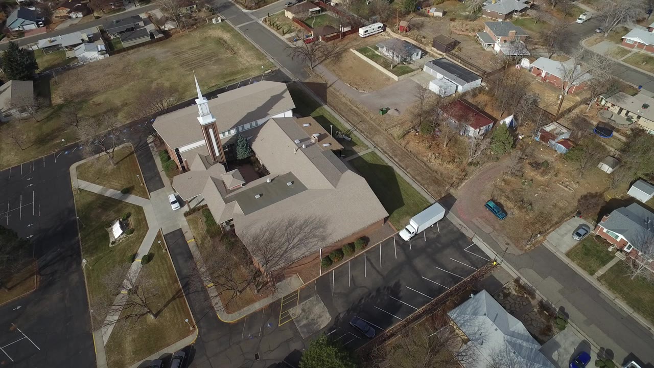 Aerial view of a church with a white steeple beside streets and parking lots.