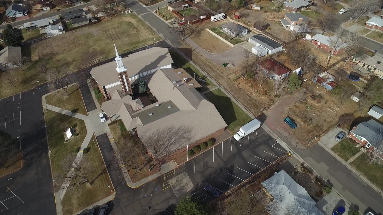 Aerial view in Westminster, Colorado showing the church steeple near the left side of the roof, empty parking rows, adjoining streets, houses, winter trees, and no visible people.