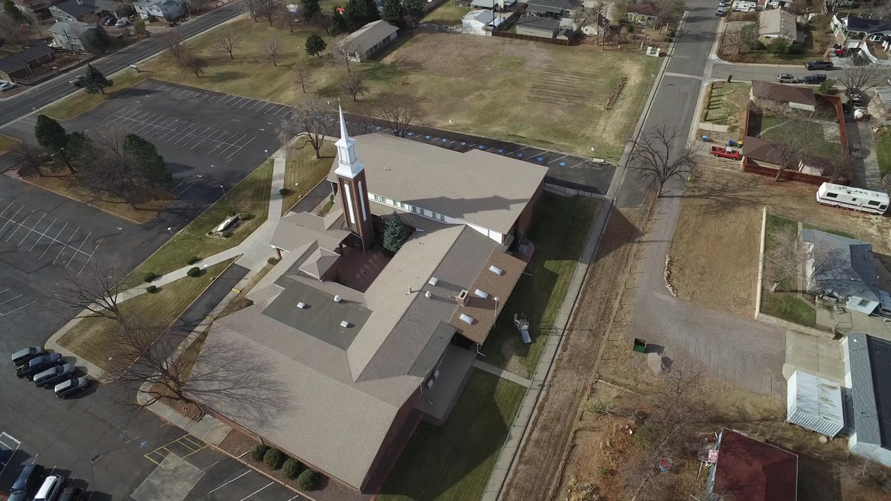 High oblique view in Westminster, Colorado with the church complex at lower left, a road running past it, open grass, small nearby buildings, houses, and no visible people.