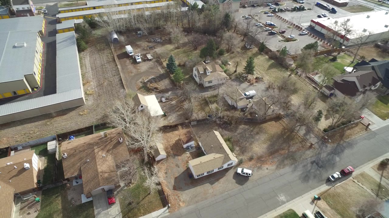 Aerial view of gray-roofed commercial buildings, homes, roads, and open lots.