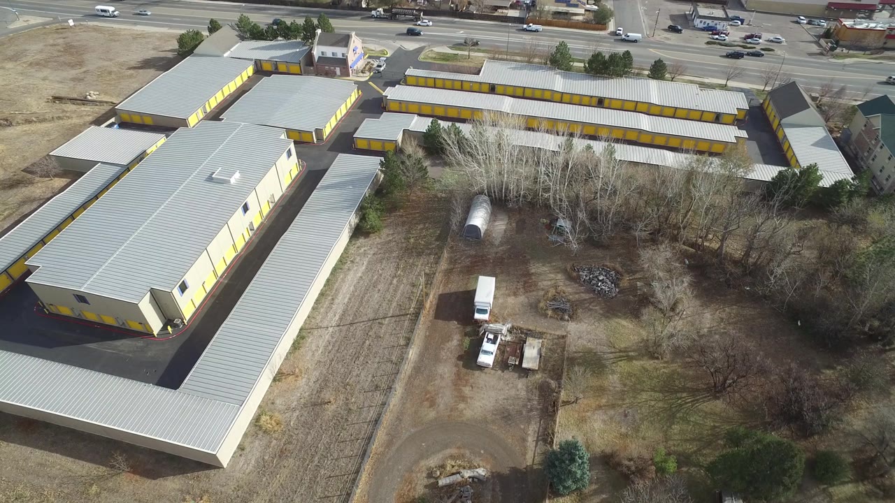 High angle frame in Westminster, Colorado with the long yellow building centered, a road with cars at the top, bare trees below, and no visible people.