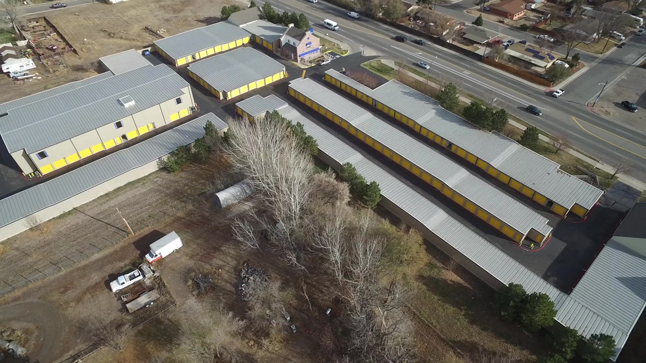 A slightly later Westminster, Colorado aerial frame shows the long storage rows, a larger gray-roofed building, passing cars on the road, houses, trees, and no visible people.