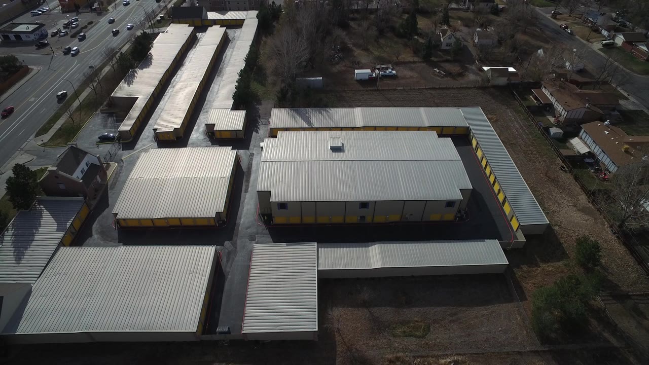 The second frame looks across the warehouse roofs and long storage-like structures in Westminster, Colorado, with moving road traffic at the edge and no visible people.