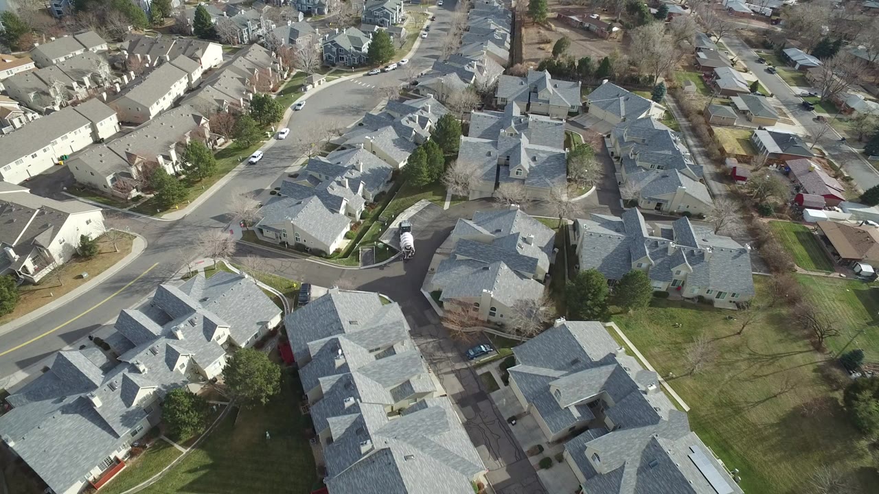 Aerial view over gray-roofed suburban homes and curved streets.