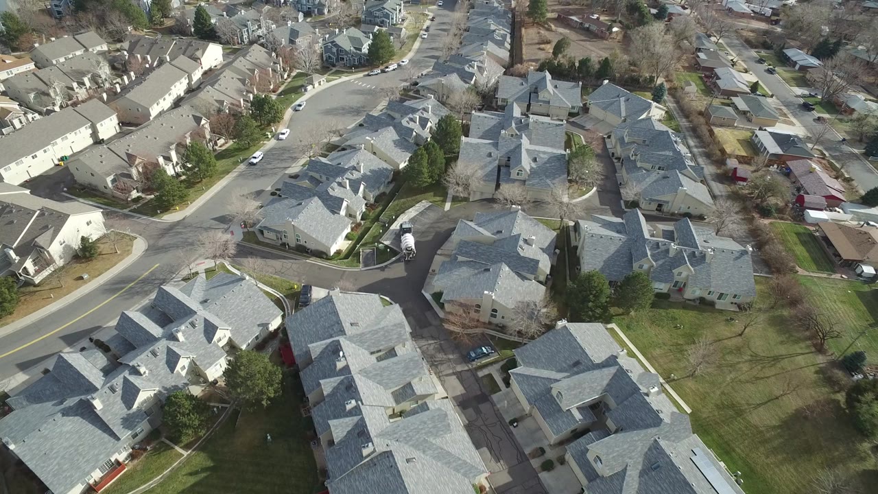 Aerial view of Westminster, Colorado residences with rows of gray roofs, small driveways, lawns, street trees, several parked cars, and no visible people.