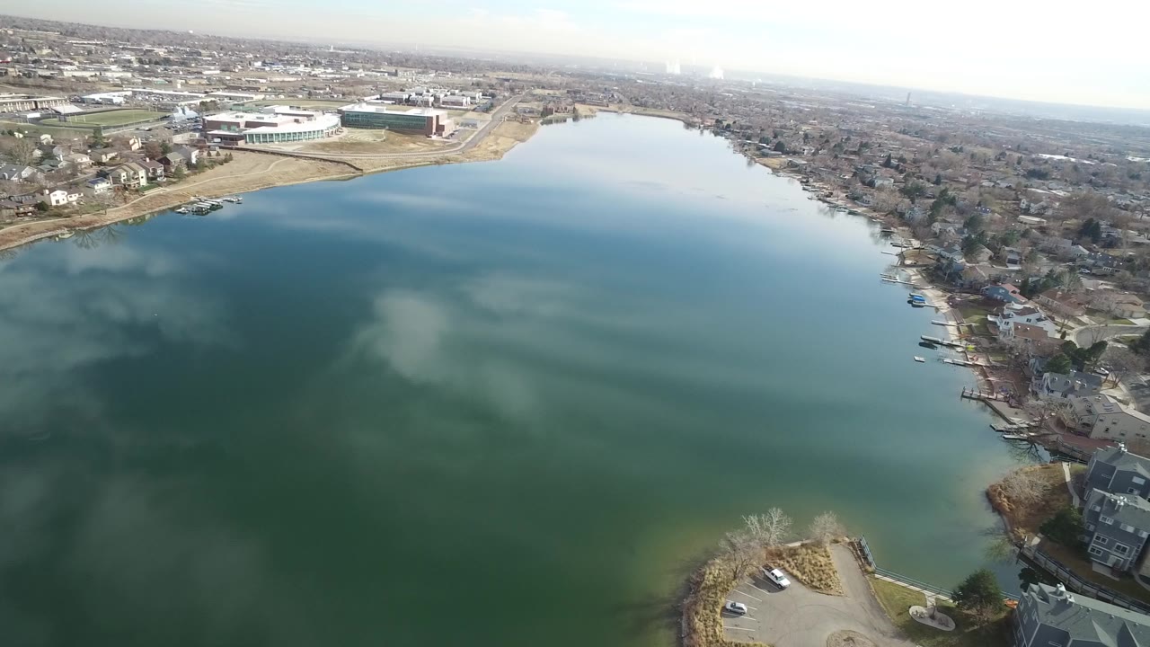 The second Westminster, Colorado frame keeps the reflective water centered while shoreline houses and small docks run down the right side, with no visible people.