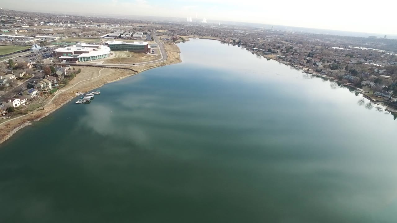 Aerial view over blue-green water beside shoreline homes and roads.