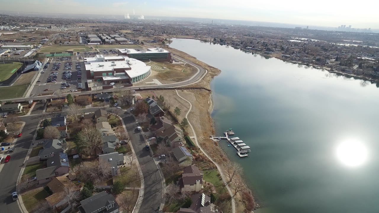 Aerial view in Westminster, Colorado with homes below, a broad lake filling the center, a small dock at the right shoreline, and no visible people.