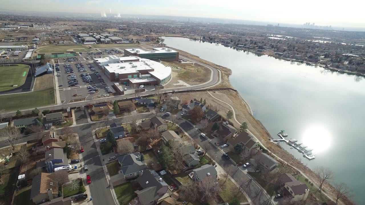 Aerial view of homes, a large building, parked cars, and a body of water.