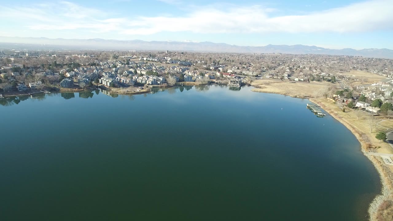 Wide aerial view over a lake toward shoreline homes and distant hills.
