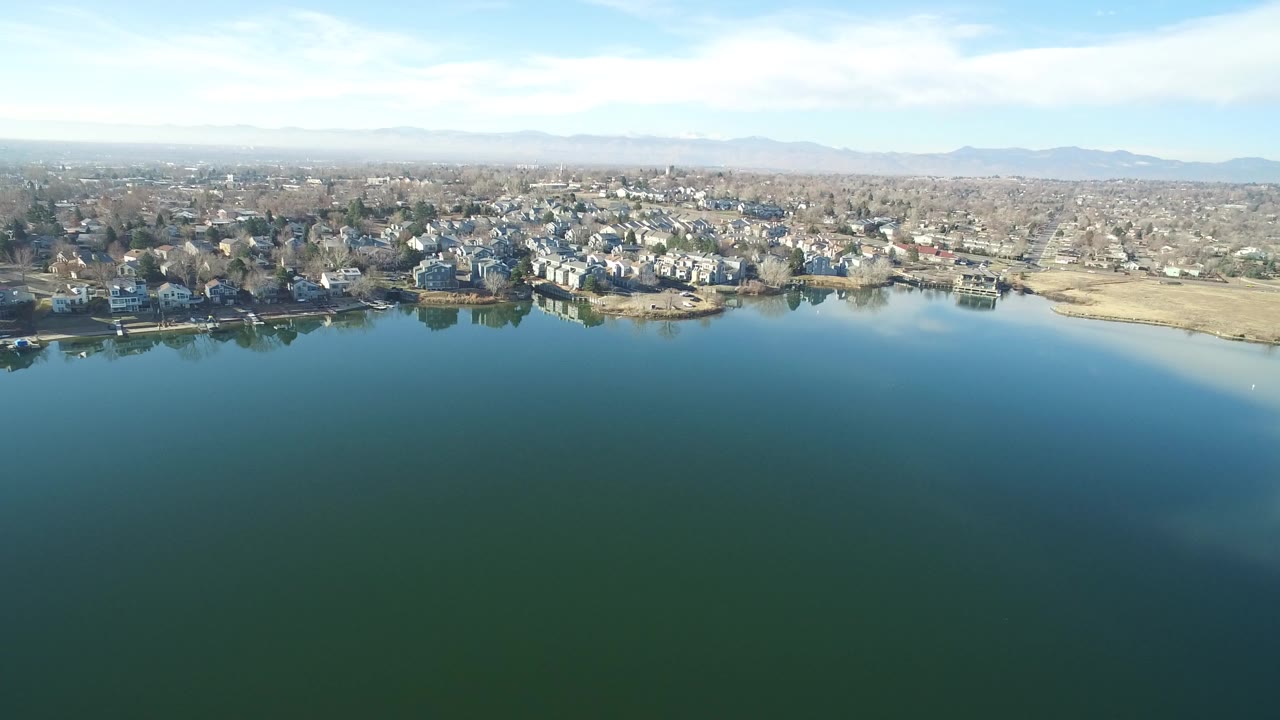 Wide aerial view over lake water toward shoreline homes and distant mountains.