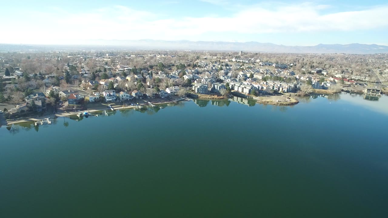 Aerial view across a lake toward shoreline homes and docks.