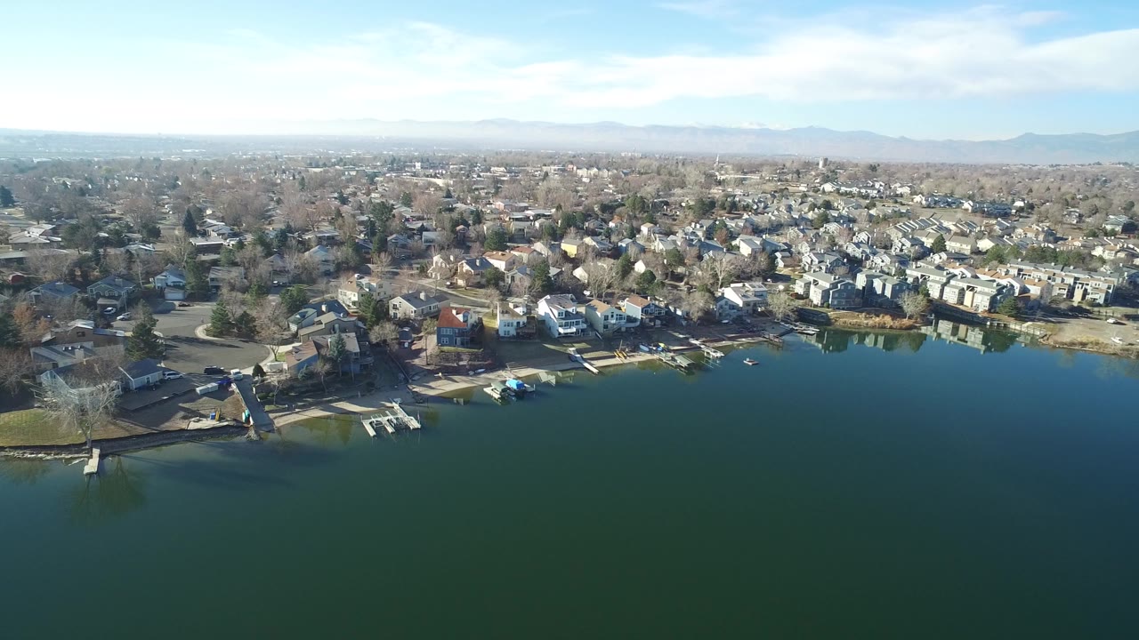 Opening aerial frame of Hidden Lake, Colorado showing green lake water, small docks, lakeside homes, bare trees, distant mountains, and no visible people.