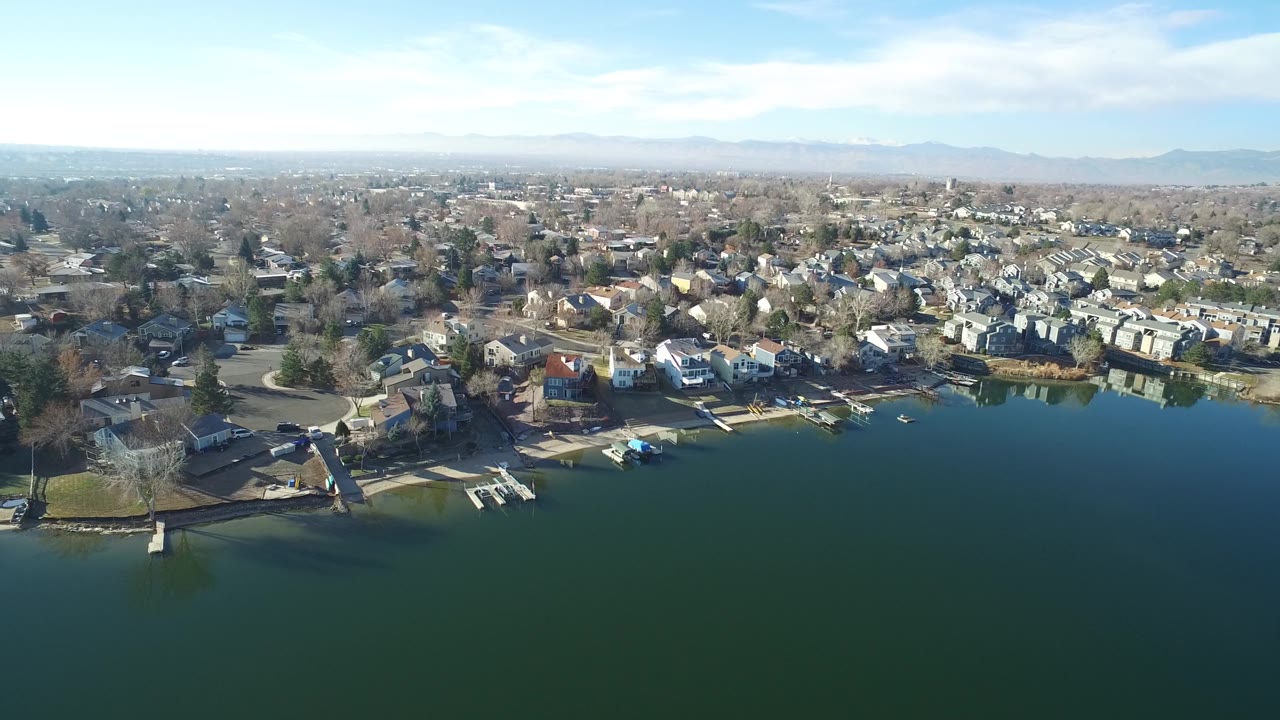 Aerial lakefront neighborhood with rows of houses and a broad mountain horizon.