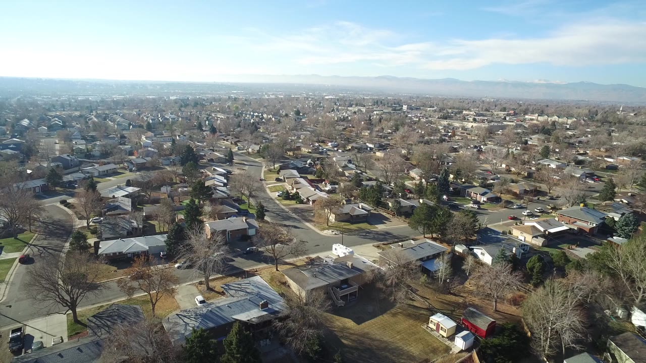 Aerial view of homes, streets, bare trees, and distant mountains.