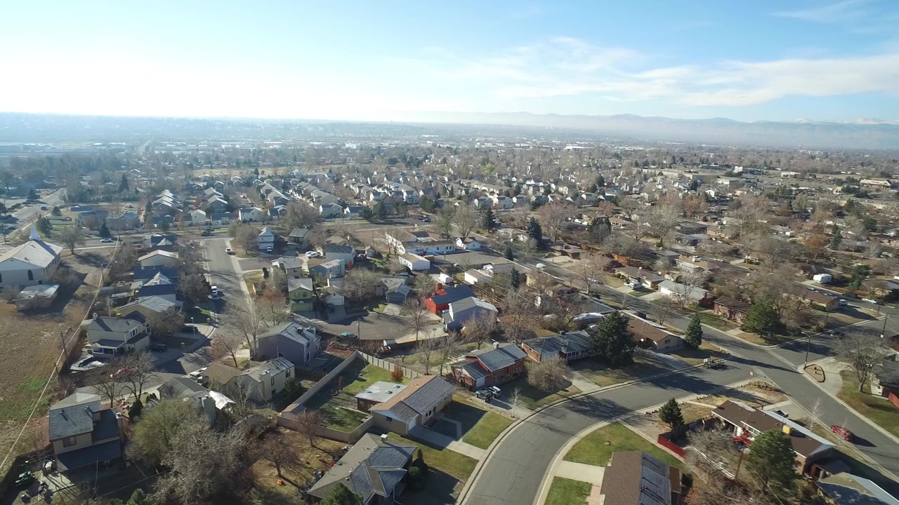 Aerial frame over Hidden Lake, Colorado showing dense detached housing, pale winter lawns, neighborhood roads, and the mountain line in the distance, with no recognizable people visible.