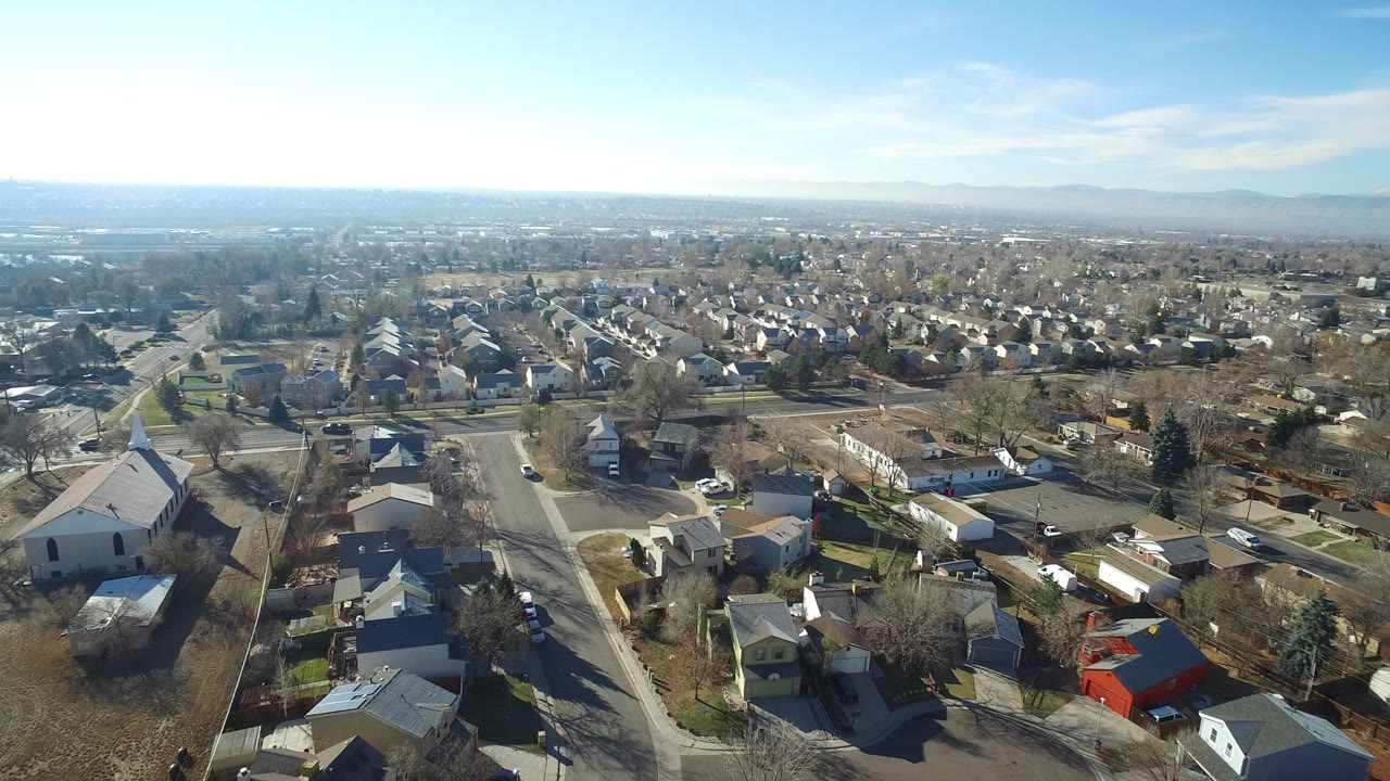 Aerial view over residential streets and rooftops under blue sky.