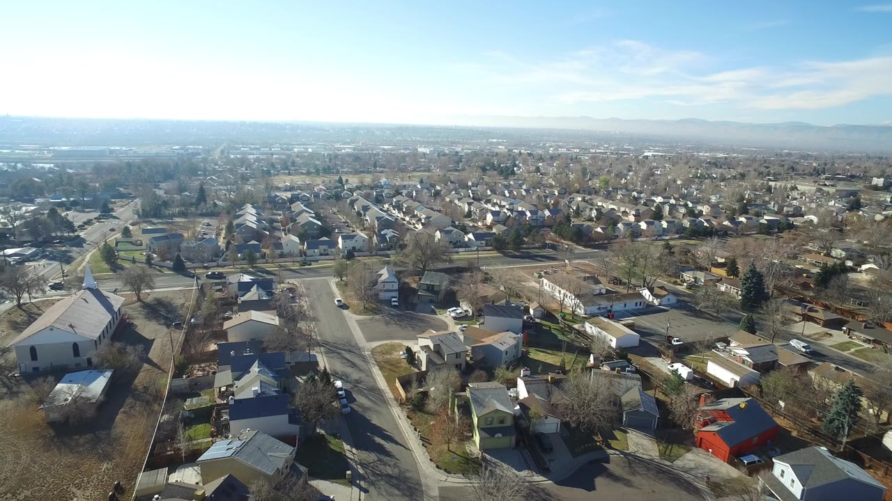 Aerial frame in Hidden Lake, Colorado with a white church-like building near the foreground, surrounding homes, cars on roads, and no visible people.