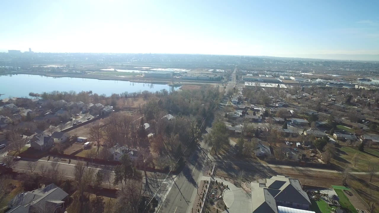 Aerial view of houses, leafless trees, roads, and water beyond the neighborhood.