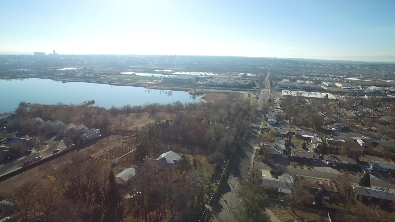 Aerial view in Hidden Lake, Colorado showing the lake shifted slightly left of center, houses and bare trees in the foreground, commercial roofs beyond the road, and no visible people.