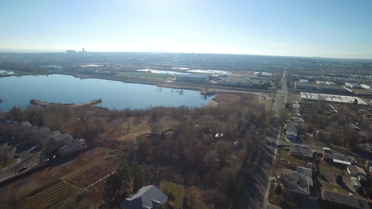Aerial view of a lake beside homes, trees, roads, and distant buildings.
