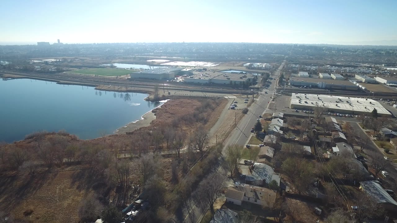Aerial view of a lake beside roads, homes, rail lines, and industrial buildings