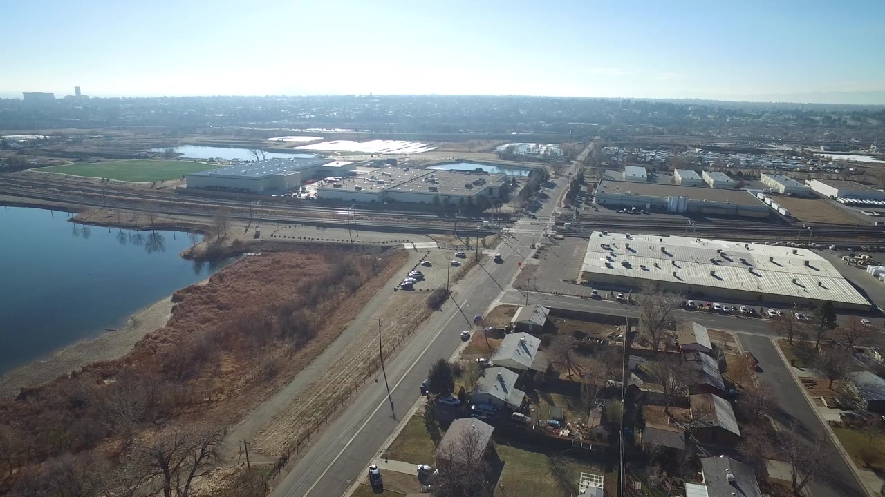 Aerial view of water, marsh, roads, rail tracks, warehouses, and nearby homes.