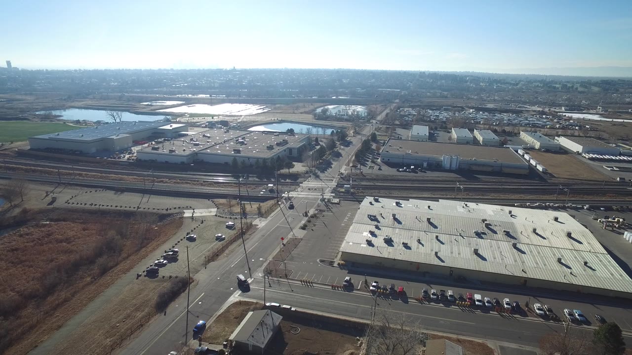 Aerial view over commercial roofs, roads, rail tracks, and distant water.