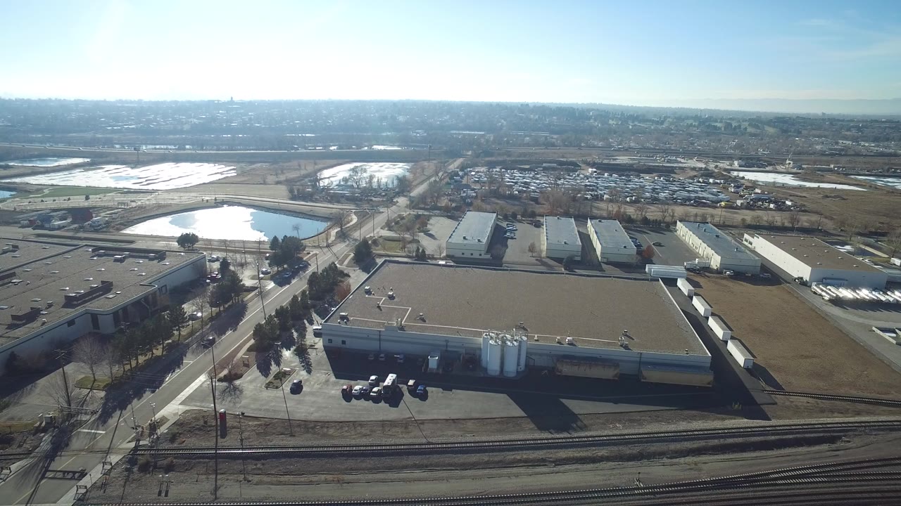 Aerial view of industrial buildings beside roads, rail tracks, and a blue lake.