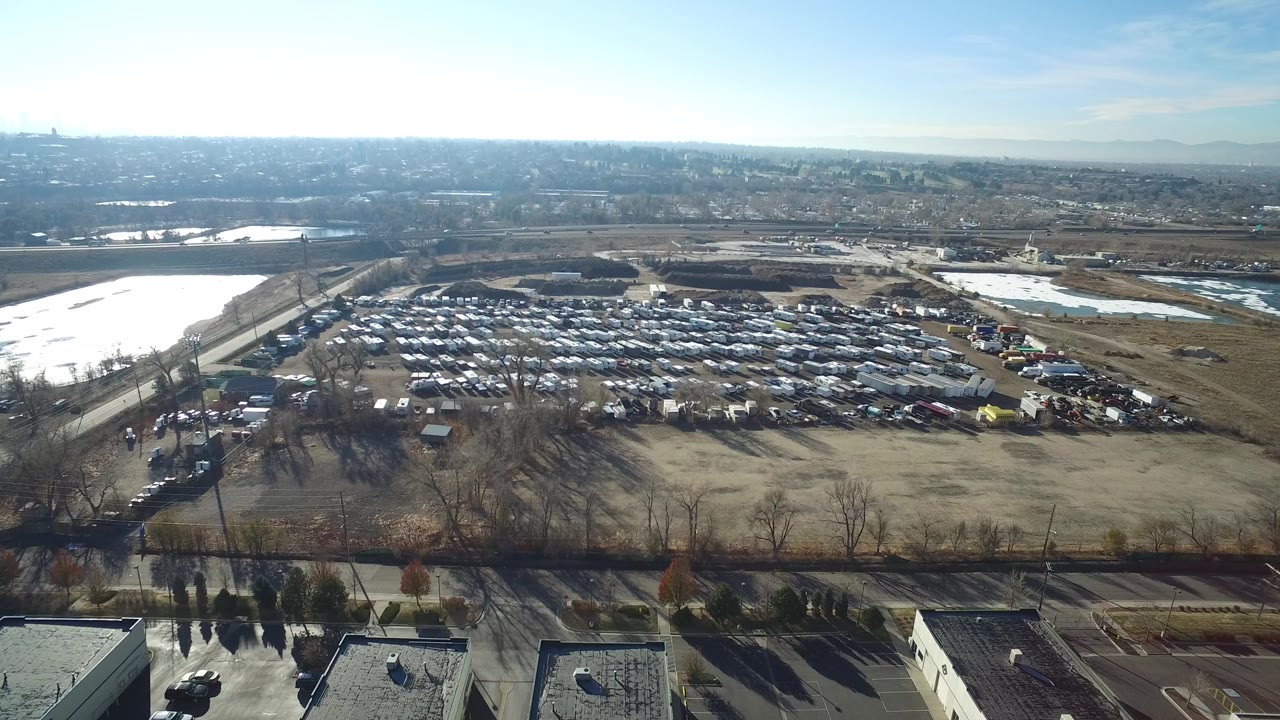 Aerial view of a large vehicle lot beside open fields and reflective water.