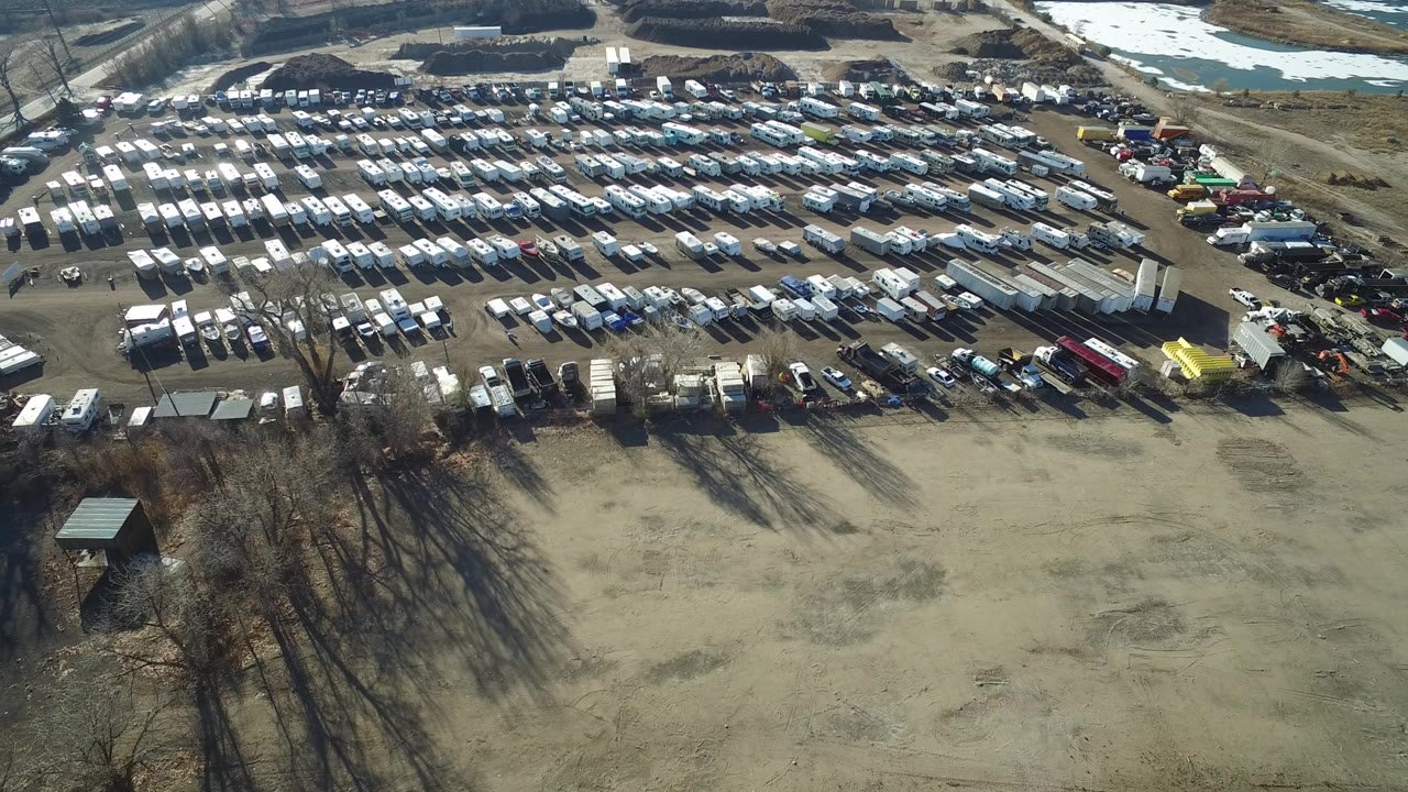 Hidden Lake, Colorado aerial frame with vehicle rows filling the upper half, tree shadows crossing the dirt lot, and no visible people.