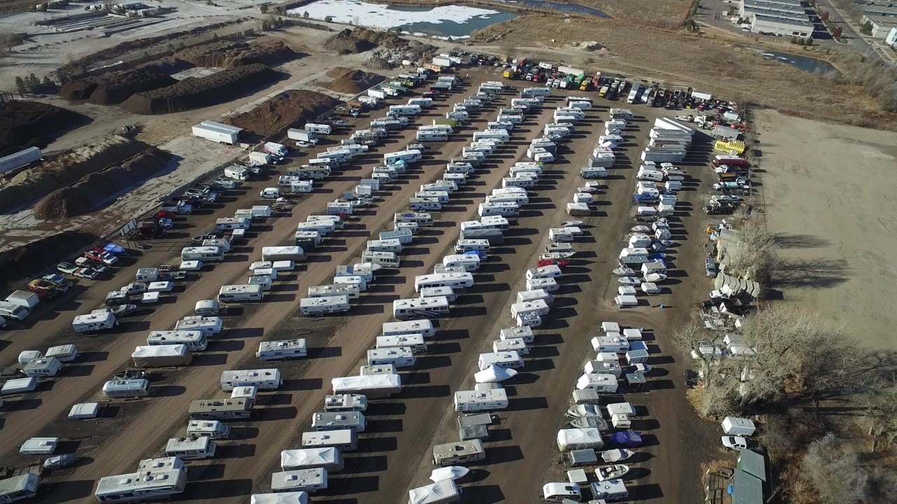 High aerial view over a full Hidden Lake, Colorado RV parking area with rows of white caravans, scattered cars, dirt lanes, and no clearly visible people.