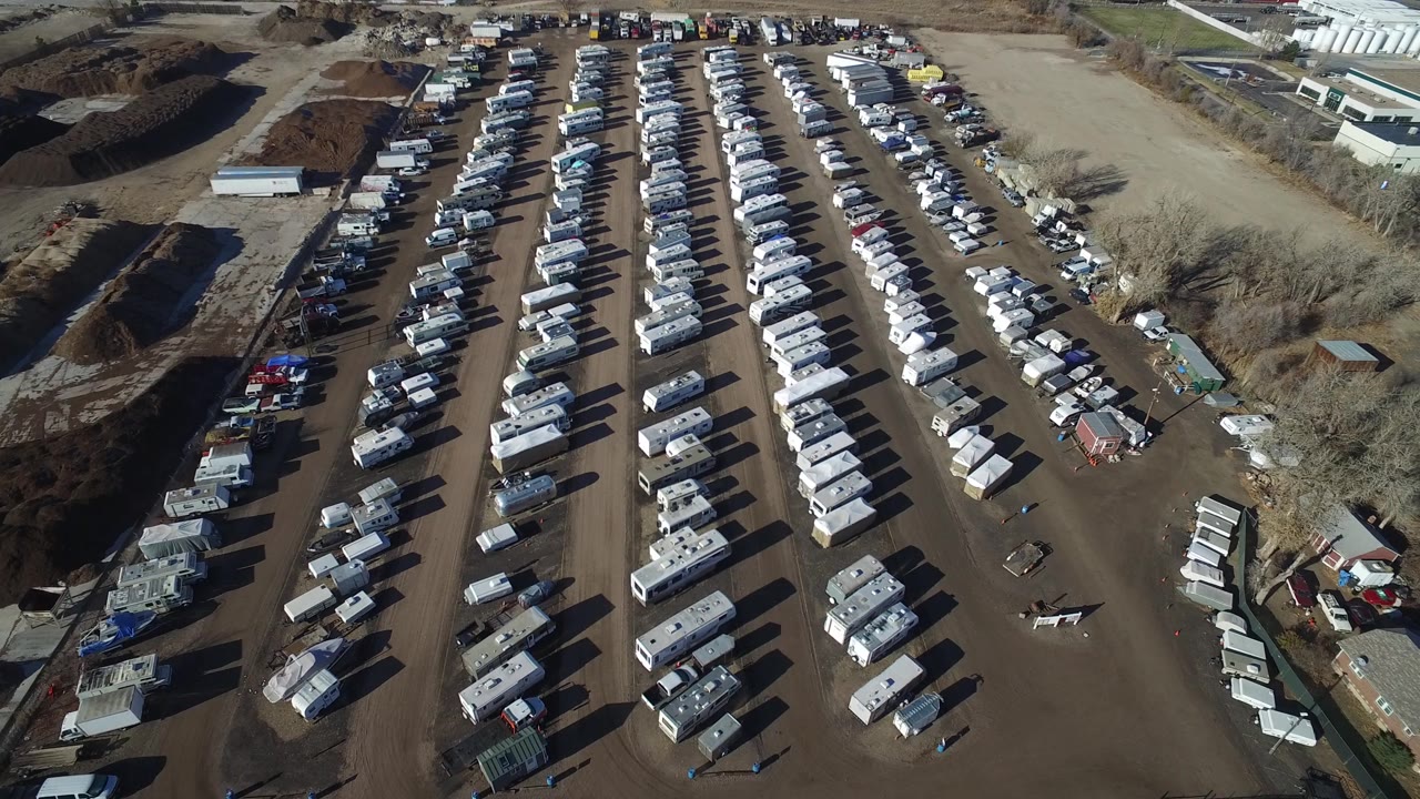 A high drone angle over Hidden Lake, Colorado frames parallel vehicle rows, dirt lanes, soil piles, and small buildings, with no visible people.