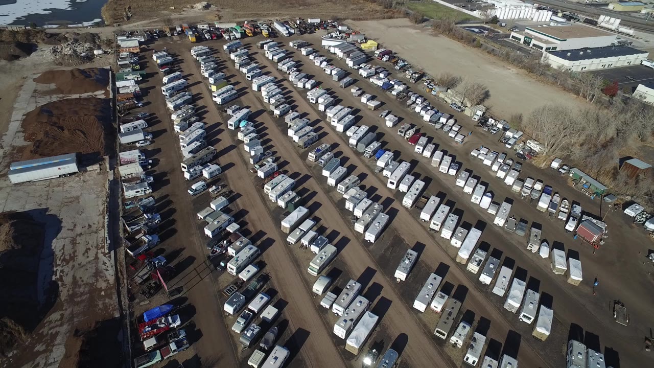 Aerial view of a crowded trailer and vehicle lot beside industrial buildings.