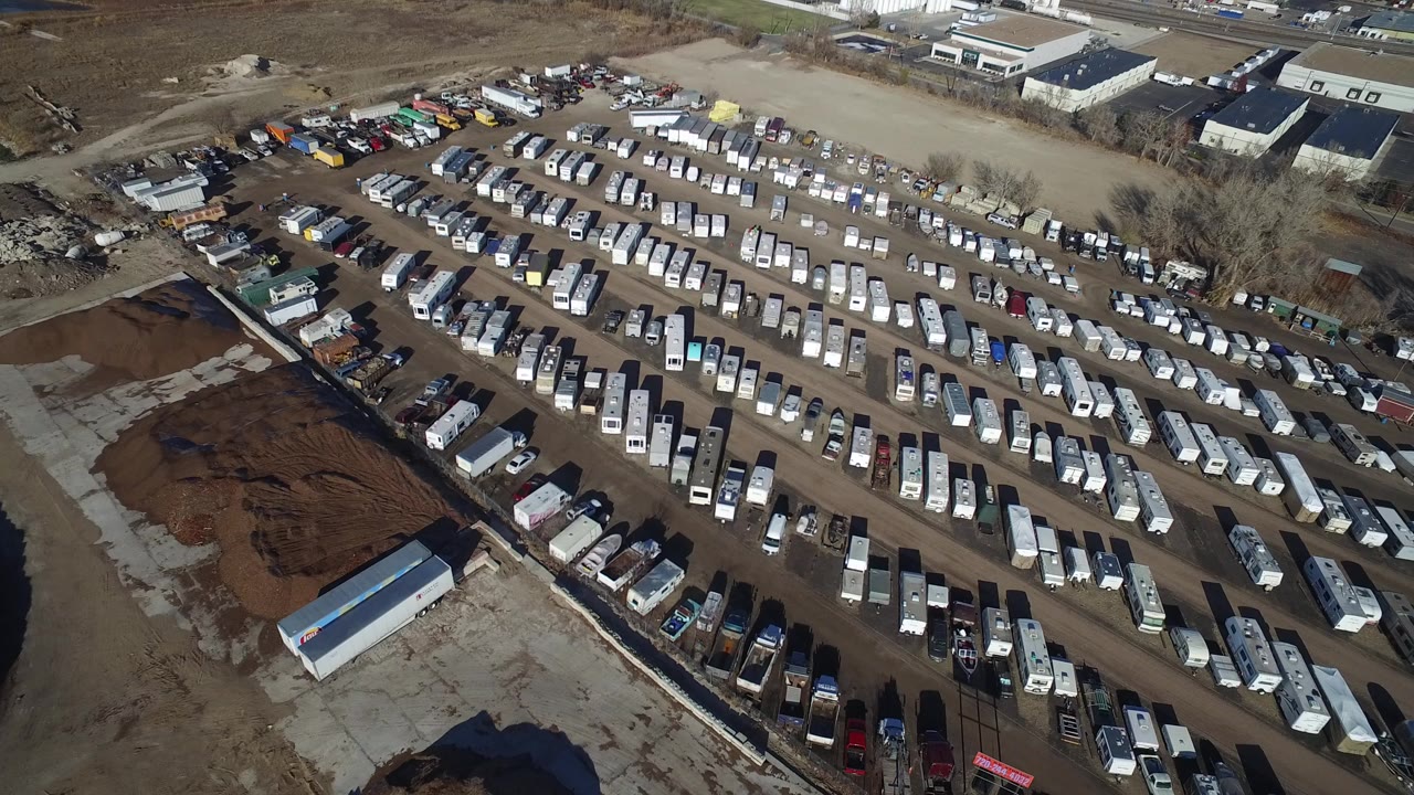 Elevated view over Hidden Lake, Colorado showing a dirt yard packed with white trailers, parked vehicles, low buildings, bare trees, and no visible recognizable people.