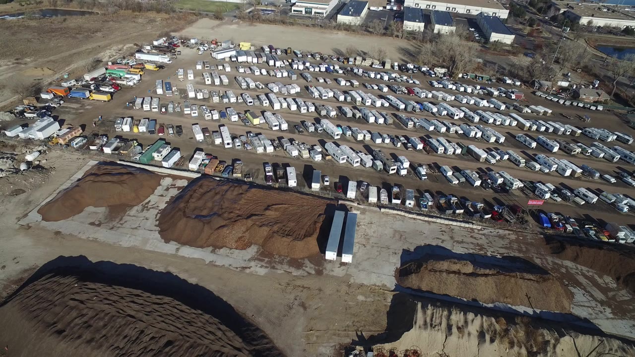 Aerial view of a gravel industrial lot with dirt piles and rows of parked vehicles.