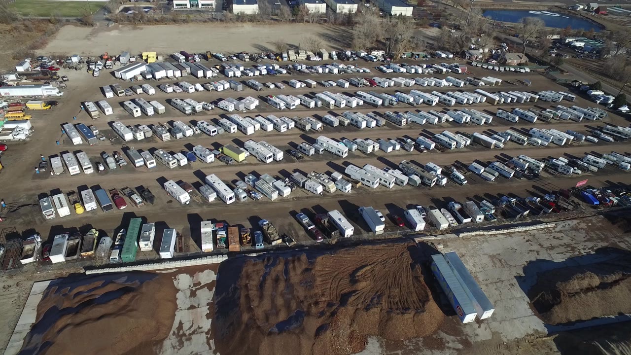 Drone view across the Hidden Lake, Colorado storage lot with dense rows of white trailers and darker parked vehicles, bordered by bare trees and low buildings, with no visible people.