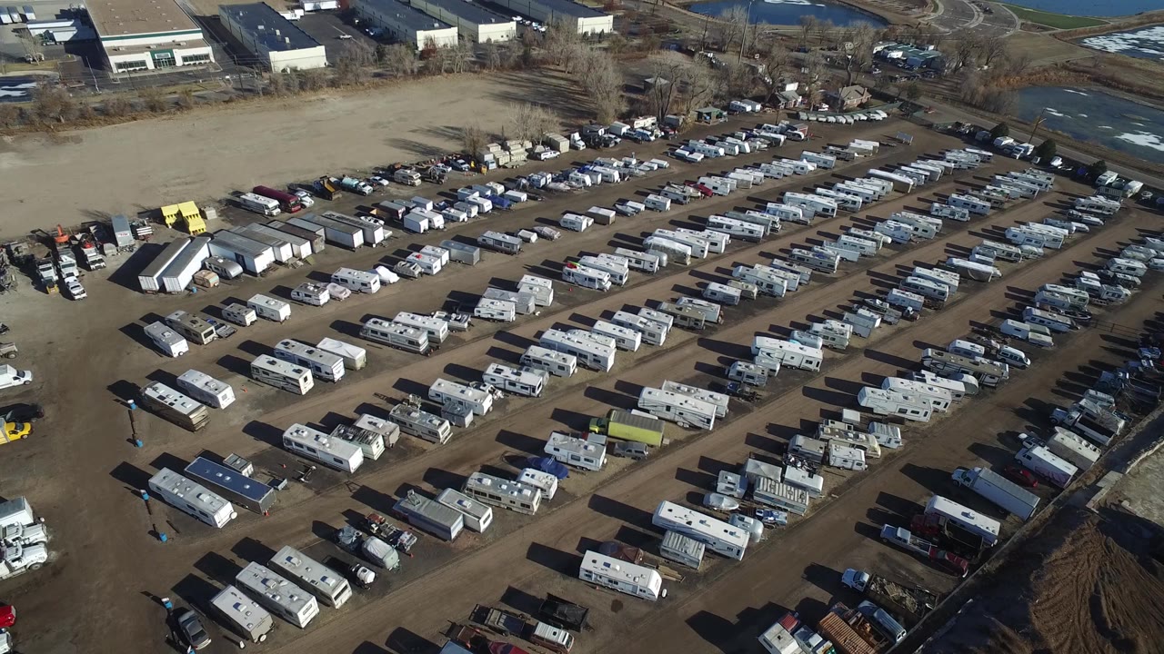 Second aerial frame in Hidden Lake, Colorado showing diagonal lanes of RVs, trailers, cars, and vans, with industrial roofs at the top of frame and no visible people.