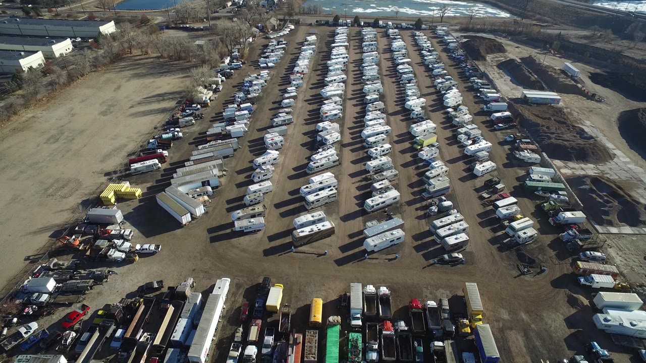 A high aerial view in Hidden Lake, Colorado, frames long rows of recreational vehicles with utility trucks and trailers along the lower edge and roads beyond the lot.