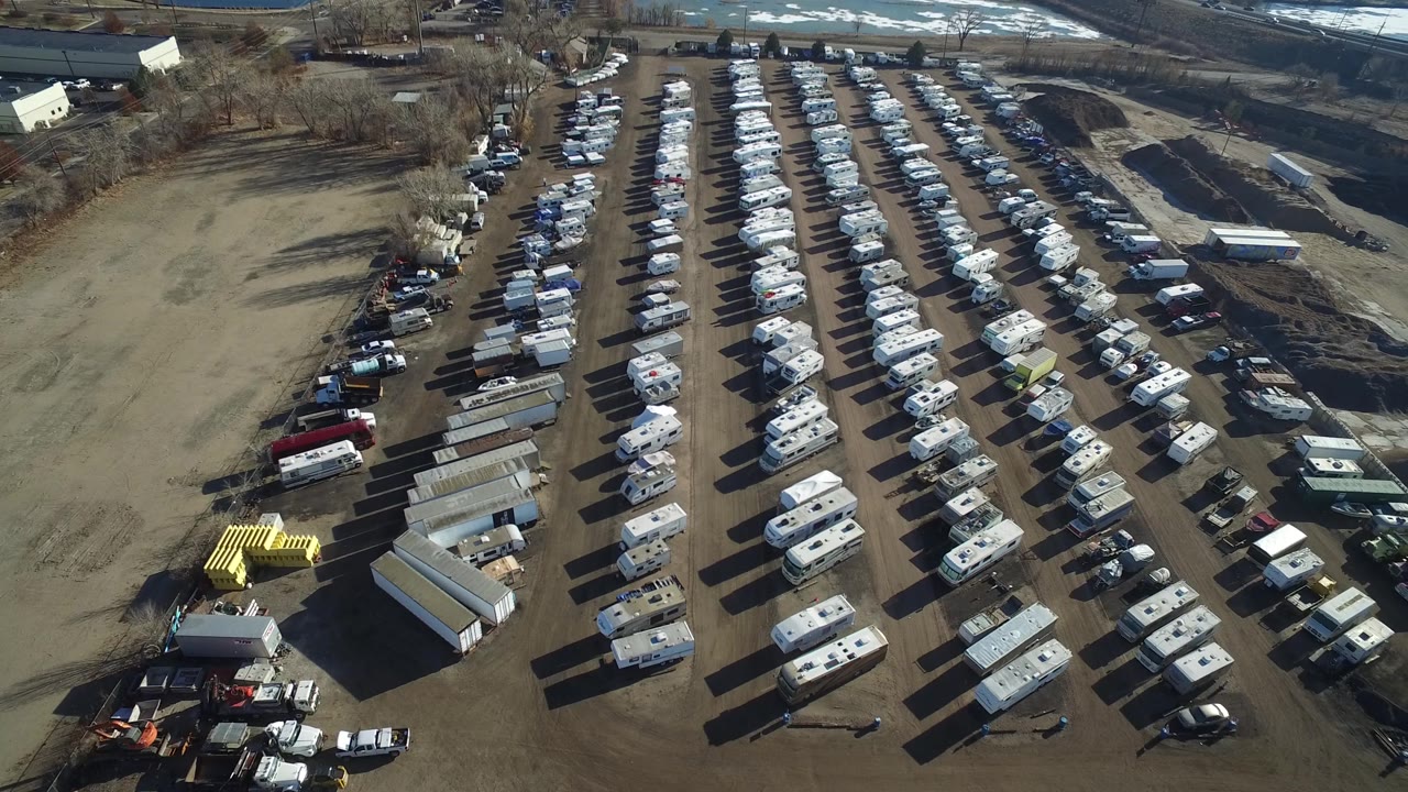 Elevated view across the Hidden Lake, Colorado campervan lot, with dense rows of RVs, a line of parked vehicles at left, sheds in the lower foreground, and no visible people.